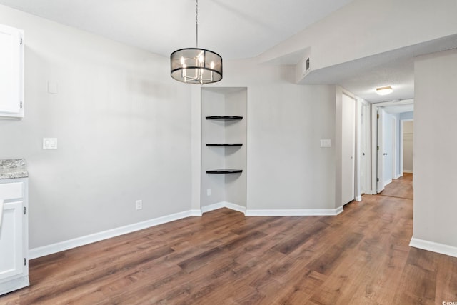 unfurnished dining area featuring baseboards, a chandelier, and wood finished floors