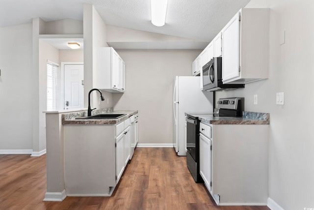 kitchen with vaulted ceiling, appliances with stainless steel finishes, a sink, and white cabinetry