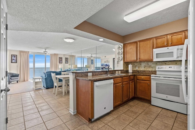 kitchen with a peninsula, white appliances, a ceiling fan, open floor plan, and brown cabinets