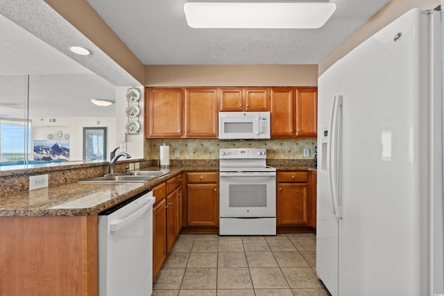 kitchen with dark countertops, white appliances, brown cabinetry, and a sink