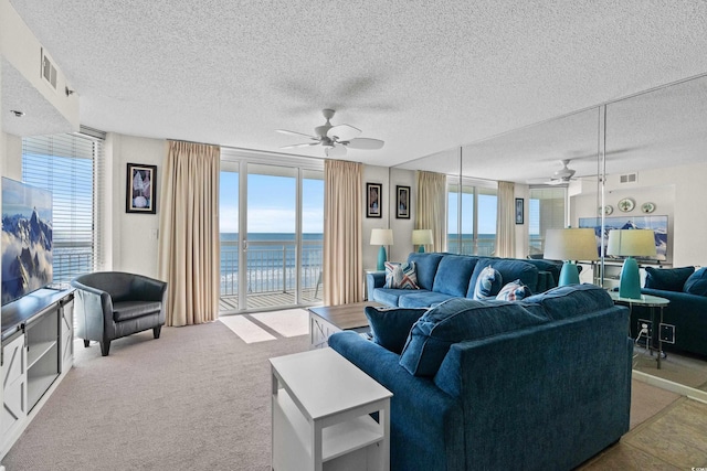 living area with a water view, carpet flooring, visible vents, and a ceiling fan