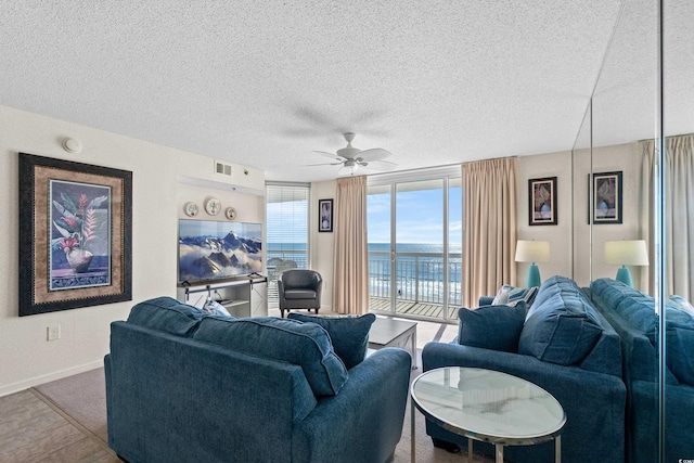 living area featuring baseboards, ceiling fan, visible vents, and a textured ceiling