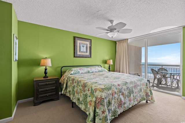 carpeted bedroom with ceiling fan, a textured ceiling, a water view, baseboards, and access to exterior