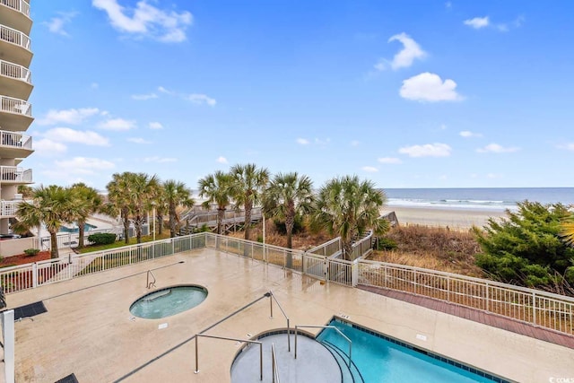 view of swimming pool with a view of the beach, a community hot tub, a water view, and fence