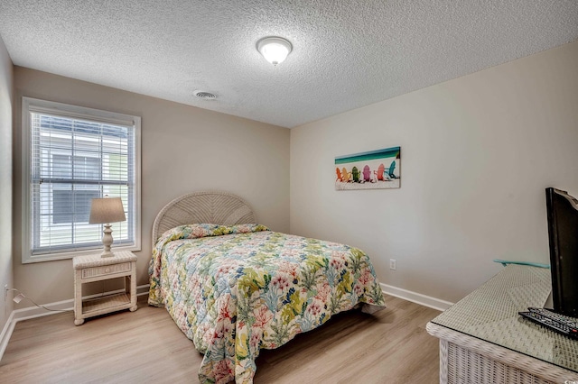 bedroom with light wood-type flooring, baseboards, visible vents, and a textured ceiling