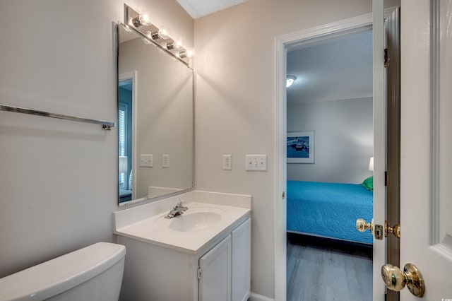 ensuite bathroom featuring toilet, a textured ceiling, vanity, and wood finished floors