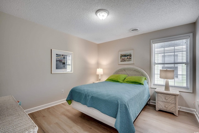 bedroom with a textured ceiling, wood finished floors, visible vents, and baseboards