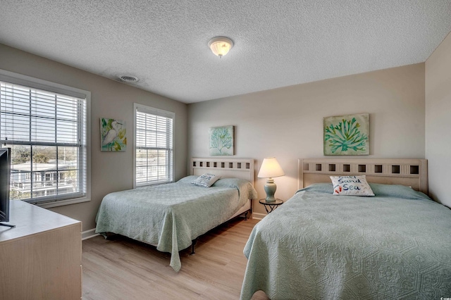 bedroom with light wood finished floors, baseboards, visible vents, and a textured ceiling