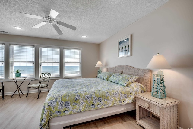 bedroom with light wood-type flooring, visible vents, baseboards, and a textured ceiling