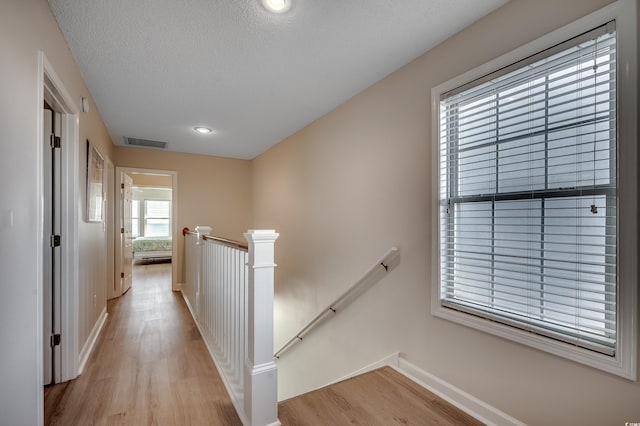 hallway featuring a textured ceiling, visible vents, an upstairs landing, baseboards, and light wood-type flooring