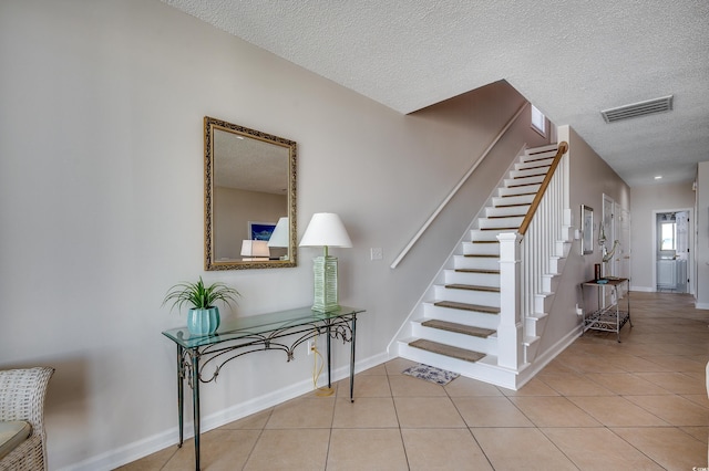 staircase featuring a textured ceiling, tile patterned flooring, visible vents, and baseboards