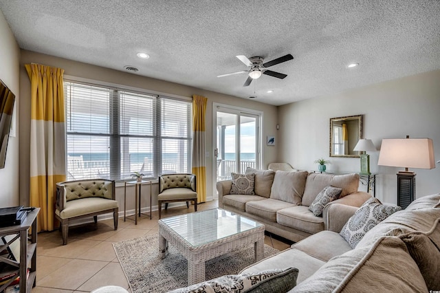 living room featuring light tile patterned floors, a ceiling fan, visible vents, and a textured ceiling