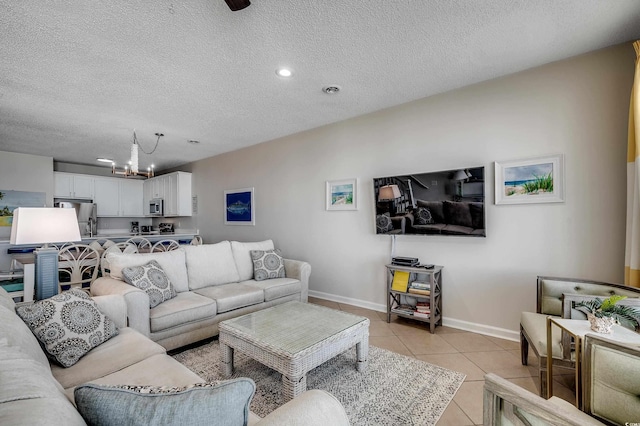 living room with light tile patterned floors, a textured ceiling, baseboards, and an inviting chandelier