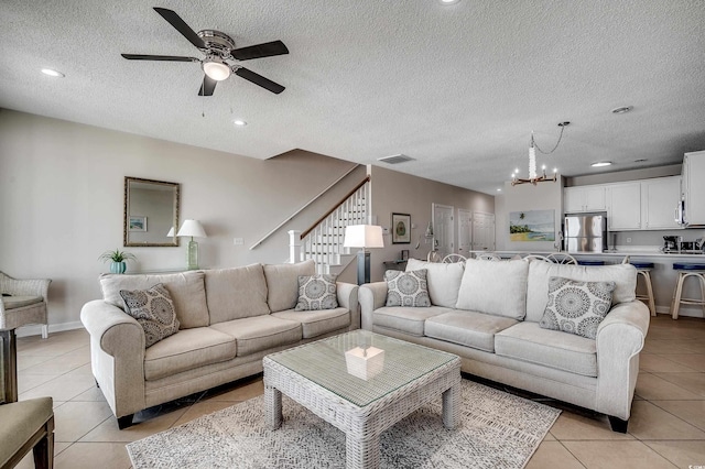 living area with light tile patterned floors, stairs, visible vents, and ceiling fan with notable chandelier