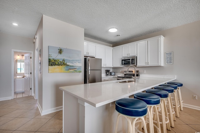 kitchen with light tile patterned floors, appliances with stainless steel finishes, a peninsula, white cabinetry, and a sink