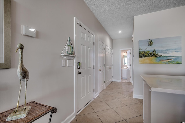 corridor featuring light tile patterned floors, baseboards, and a textured ceiling