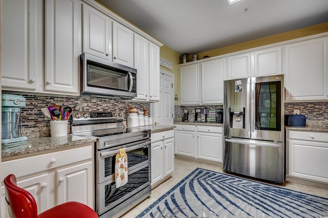 kitchen with light tile patterned floors, tasteful backsplash, white cabinetry, light stone counters, and stainless steel appliances