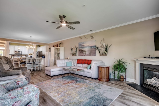 living room with ornamental molding, wood finished floors, a fireplace with flush hearth, and ceiling fan with notable chandelier
