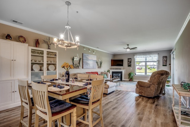 dining space with ornamental molding, visible vents, light wood-style flooring, and ceiling fan with notable chandelier