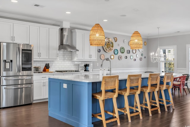 kitchen featuring an island with sink, wall chimney range hood, ornamental molding, and stainless steel appliances