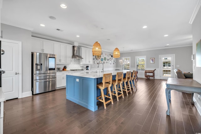 kitchen featuring gas stovetop, visible vents, wall chimney range hood, stainless steel refrigerator with ice dispenser, and a kitchen bar