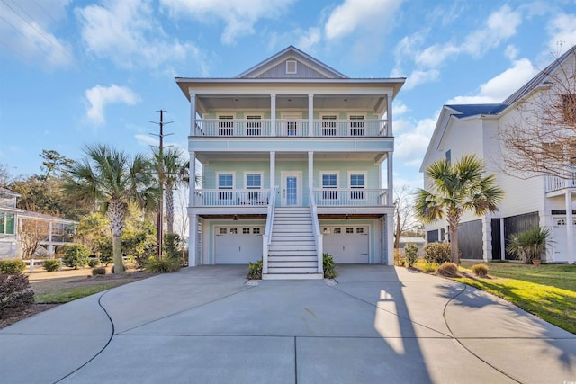 beach home with a porch, a balcony, a garage, concrete driveway, and stairway