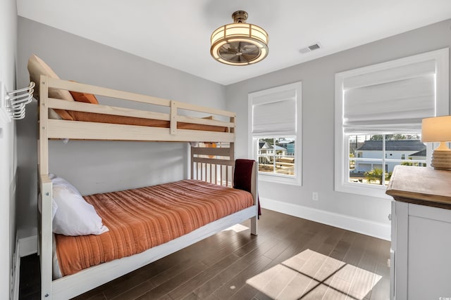 bedroom with dark wood-style floors, visible vents, multiple windows, and baseboards