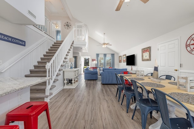 dining room featuring visible vents, a ceiling fan, a wainscoted wall, wood finished floors, and stairs