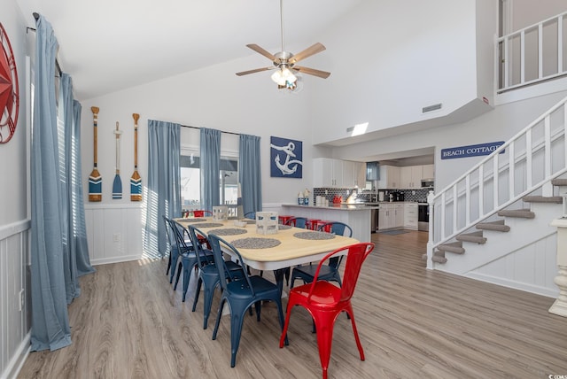 dining room featuring ceiling fan, high vaulted ceiling, visible vents, light wood-style floors, and stairway