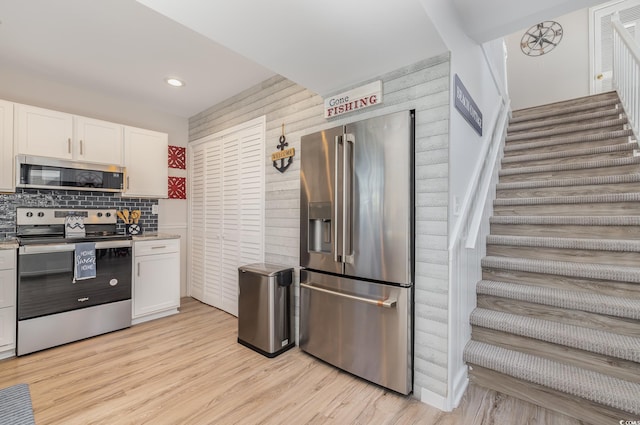 kitchen with light wood-type flooring, appliances with stainless steel finishes, white cabinets, and decorative backsplash