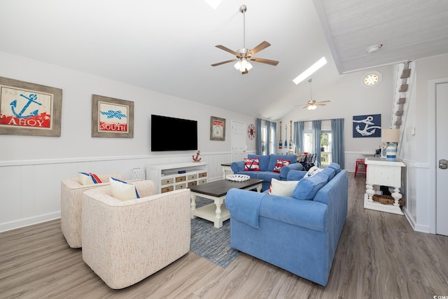 living area with a wainscoted wall, vaulted ceiling with skylight, wood finished floors, and a ceiling fan