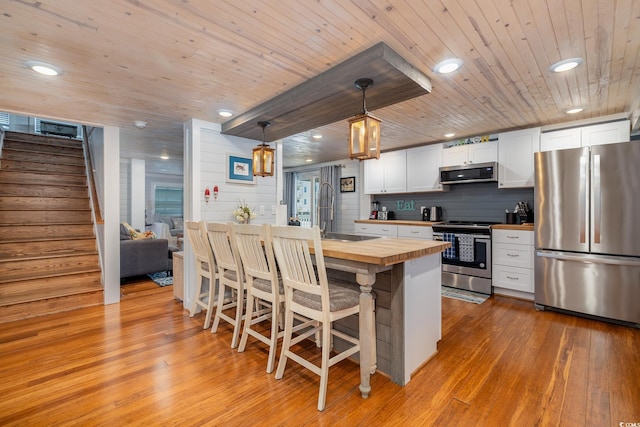 kitchen with stainless steel appliances, a sink, butcher block countertops, light wood-type flooring, and wooden ceiling