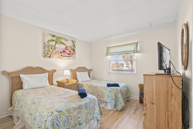 bedroom featuring a textured ceiling, wood finished floors, attic access, and baseboards