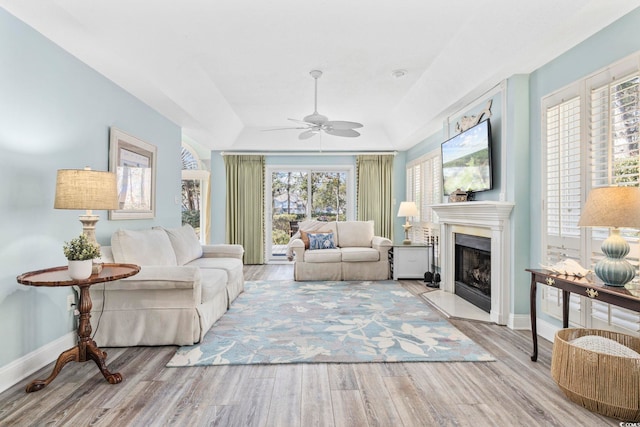 living area with a ceiling fan, a fireplace with raised hearth, baseboards, and wood finished floors