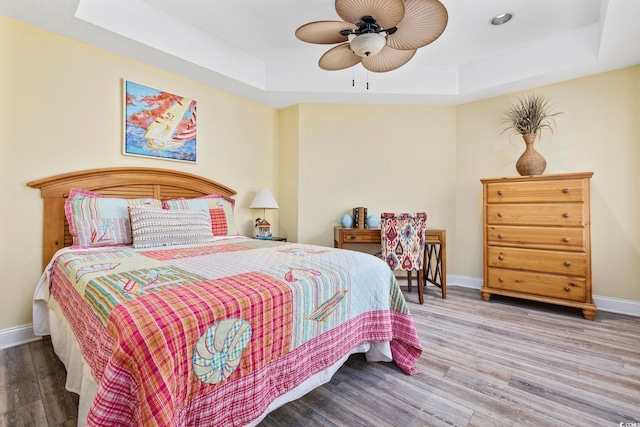 bedroom with wood finished floors, a raised ceiling, and baseboards