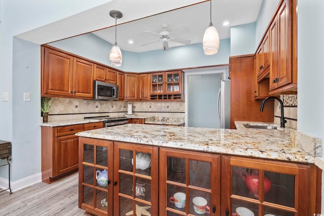 kitchen with a peninsula, a sink, appliances with stainless steel finishes, light stone countertops, and brown cabinetry