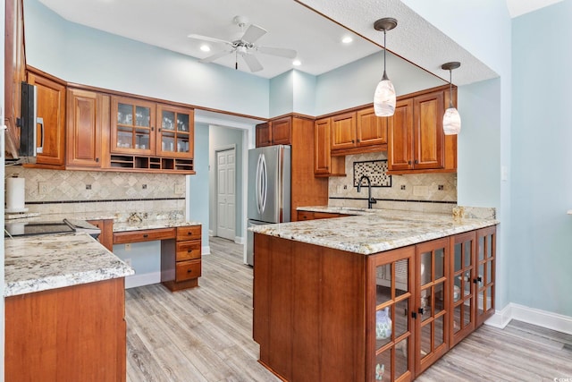 kitchen with a peninsula, a sink, brown cabinets, freestanding refrigerator, and light stone countertops