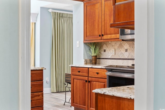 kitchen with tasteful backsplash, stainless steel electric stove, brown cabinetry, and light stone counters