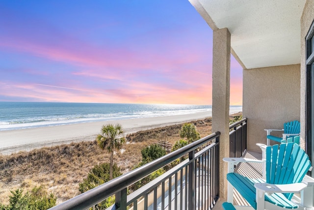 balcony at dusk featuring a water view and a beach view