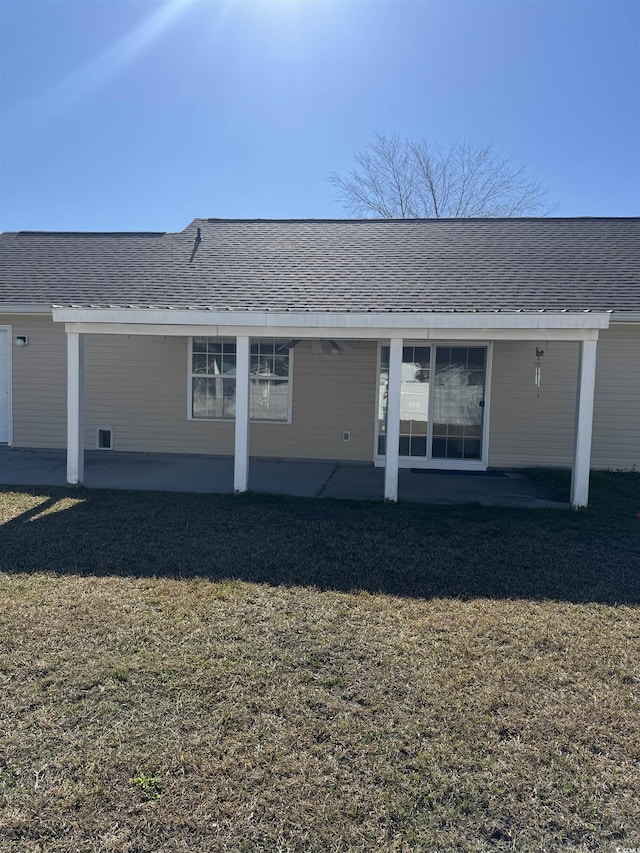 rear view of house with roof with shingles, a lawn, and a patio