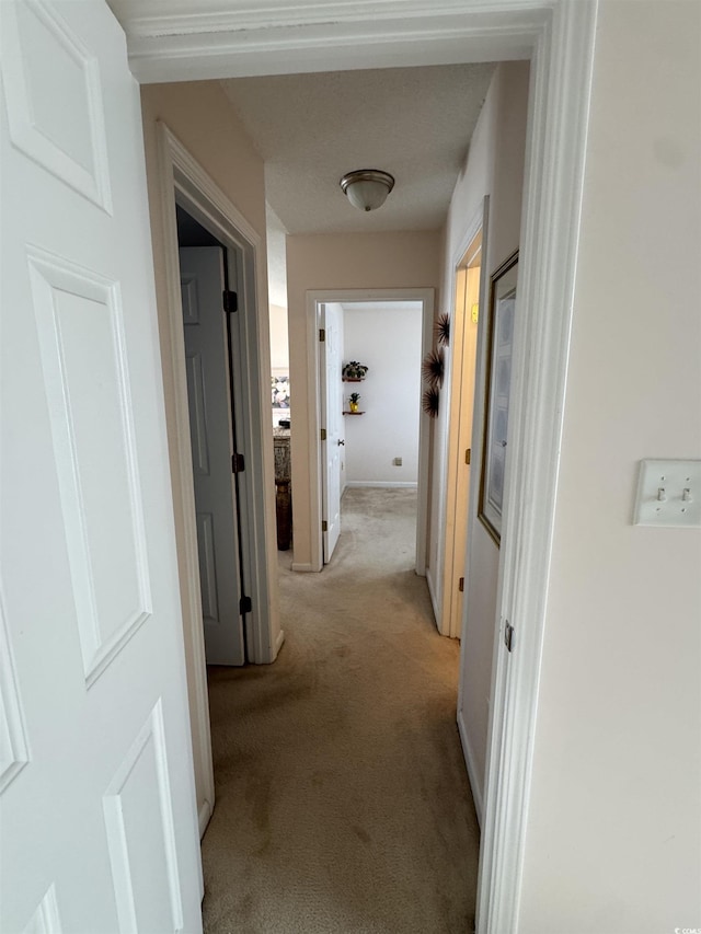 hallway with baseboards and light colored carpet