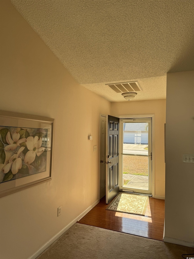 carpeted entrance foyer with baseboards, visible vents, a textured ceiling, and wood finished floors