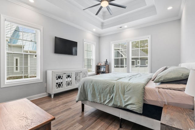 bedroom with wood finished floors, multiple windows, a raised ceiling, and crown molding