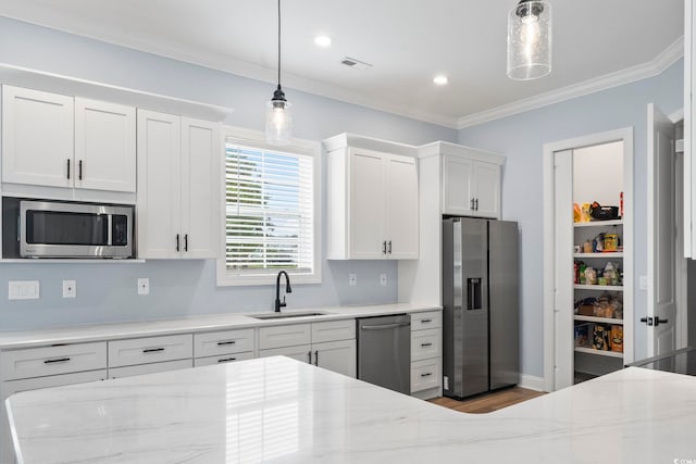 kitchen featuring white cabinets, light stone counters, ornamental molding, stainless steel appliances, and a sink