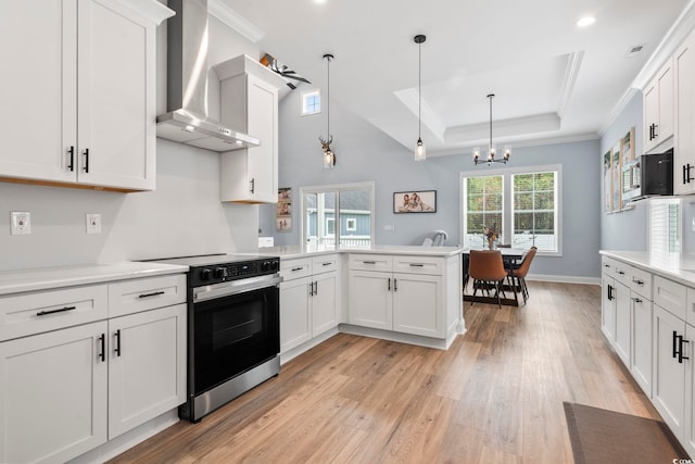 kitchen featuring a raised ceiling, electric stove, wall chimney exhaust hood, stainless steel microwave, and a peninsula