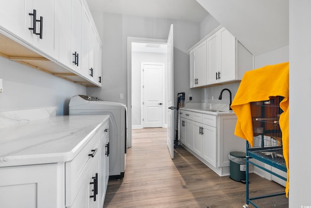 washroom with wood finished floors, washing machine and clothes dryer, a sink, and cabinet space