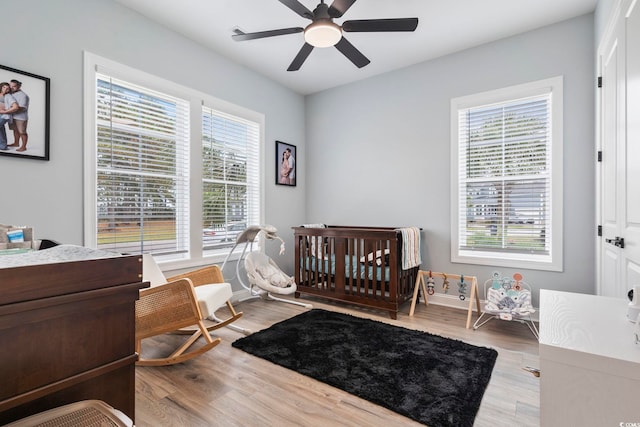 bedroom with a nursery area, ceiling fan, and wood finished floors