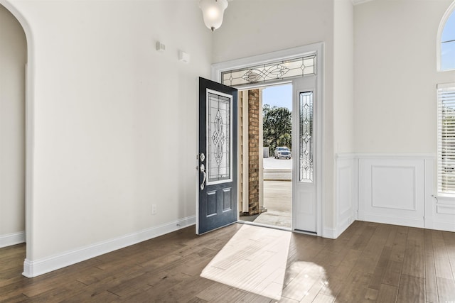 foyer with arched walkways, wainscoting, dark wood-style floors, a high ceiling, and a decorative wall