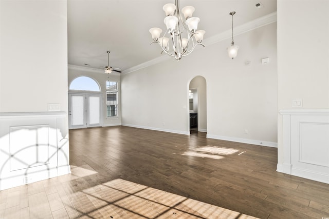 unfurnished living room with arched walkways, baseboards, wood-type flooring, ornamental molding, and ceiling fan with notable chandelier