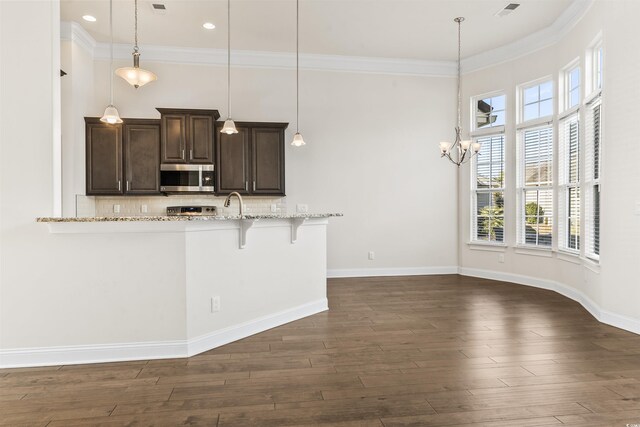 kitchen featuring dark brown cabinetry, tasteful backsplash, dark wood finished floors, stainless steel microwave, and a kitchen breakfast bar